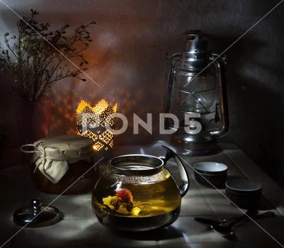 Glass teapot with blooming green tea on white table and dark background still Stock Photos