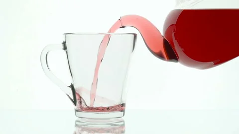 Glass teapot pouring fruit tea into cup on white background Stock Footage 96992020
