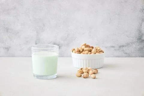A glass of vegetable milk from nuts on the table next to pistachios. The perfect Stock Photos