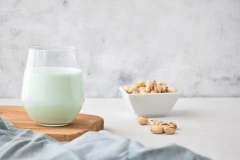 A glass of vegetable milk from nuts on the table next to pistachios. The perfect Stock Photos