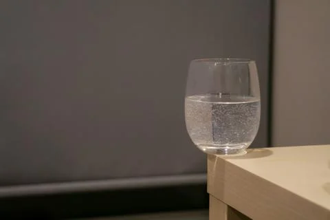 A glass of water with bubbles inside is on the corner of light yellow wooden  Foto stock