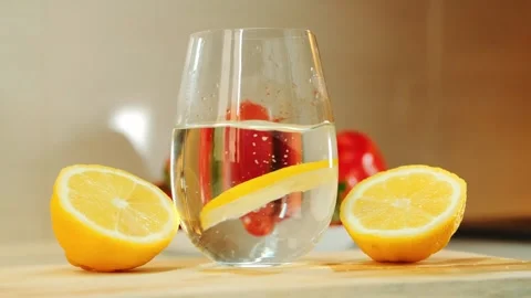 Glass of water with floating lemon slice between lemon halves on wooden board Video stock 342602220