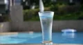 Glass of Water with Ice Cubes on Side of Blue Swimming Pool HD Footage