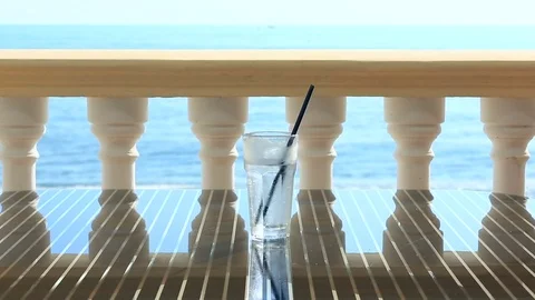 Glass of water with ice on the restaurant table overlooking the sea. Against the Stock Footage 77075461