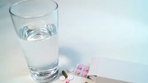 A glass of water, a number of multi-colored tablets and a box with a blister Stock Footage 201231192