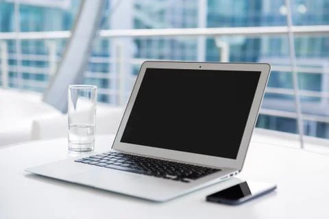 Glass of water, phone and laptop on white table in bright office. Stock Photos