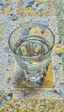 Glass with water placed on a quilt with a patchwork design. 스톡 사진
