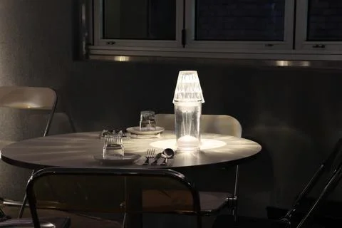 A glass of water sits on a table next to a lamp Stock Photos