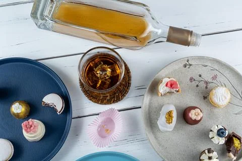 Glass of whiskey with ice surrounded by assorted wedding candies top view. Stock Photos