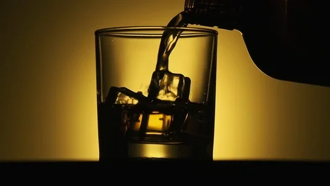 Glass with whiskey rotating at wooden table. Close-up of whiskey with ice Stock Footage 123794053