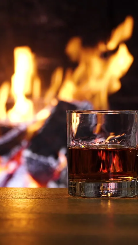 Glass of whiskey on table with fireplace flames in background Stockbeeldmateriaal 334385070
