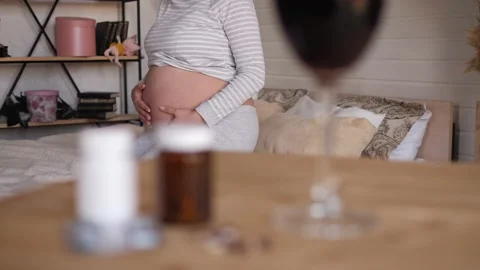 A glass of wine and pills on the table, pregnant is sitting in the background Stock Footage 134587656