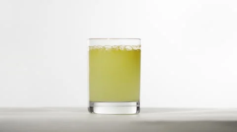 A glass of yellow liquid bubbles in front of a white BG. Stock Footage 64894542