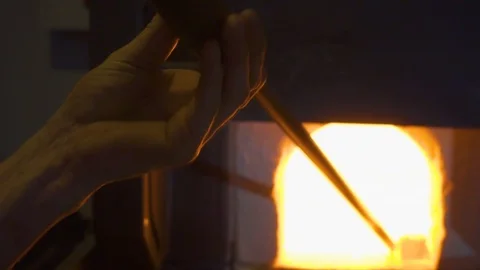 Glassblower in his workshop and rotating rod with liquid glass. Close-up. Stock Footage 109716055