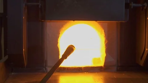 Glassblower in his workshop taking the rod with liquid glass out of glowing hot Stock Footage 108990786