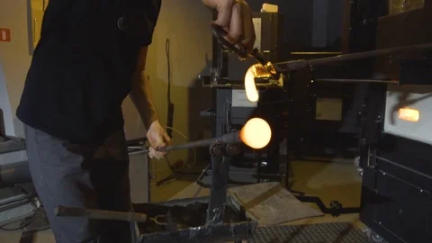 Glassblower in his workshop taking the rod with liquid glass out of glowing hot Stock Footage 108991225