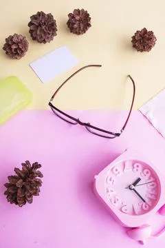 Glasses, alarm clock, pine tree flowers on a pastel pink and pastel yellow ba Stock Photos