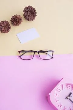 Glasses, alarm clock, pine tree flowers on a pastel pink and pastel yellow ba Stock Photos