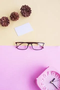 Glasses, alarm clock, pine tree flowers on a pastel pink and pastel yellow ba Stock Photos