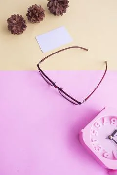 Glasses, alarm clock, pine tree flowers on a pastel pink and pastel yellow ba Stock Photos