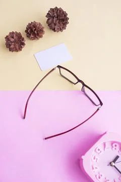 Glasses, alarm clock, pine tree flowers on a pastel pink and pastel yellow ba Stock Photos