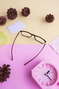 Glasses, alarm clock, pine tree flowers on a pastel pink and pastel yellow ba Stock Photos