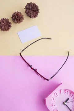 Glasses, alarm clock, pine tree flowers on a pastel pink and pastel yellow ba Stock Photos