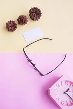 Glasses, alarm clock, pine tree flowers on a pastel pink and pastel yellow ba Stock Photos