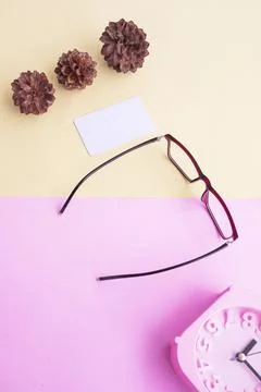 Glasses, alarm clock, pine tree flowers on a pastel pink and pastel yellow ba Stock Photos