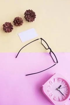 Glasses, alarm clock, pine tree flowers on a pastel pink and pastel yellow ba Stock Photos