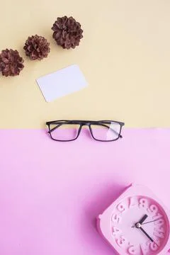 Glasses, alarm clock, pine tree flowers on a pastel pink and pastel yellow ba Stock Photos