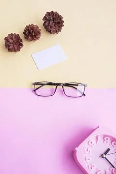 Glasses, alarm clock, pine tree flowers on a pastel pink and pastel yellow ba Stock Photos
