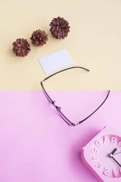 Glasses, alarm clock, pine tree flowers on a pastel pink and pastel yellow ba Stock Photos