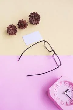 Glasses, alarm clock, pine tree flowers on a pastel pink and pastel yellow ba Stock Photos