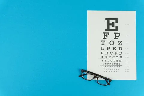 Glasses and a vision test table on the right on a blue background Stock Photos