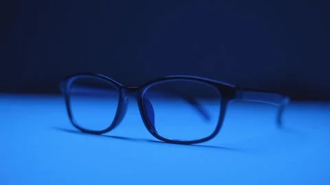 Glasses in a black frame lie on a table under blue lighting Video stock 244599363
