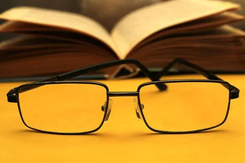 Glasses in a black frame on a yellow background. In the background is an open Stock Photos