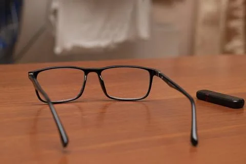 Glasses with black frames rest on a wood table next to a case in the daytime Stock Photos