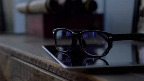 Glasses in black rim lying on a tablet on a wooden dresser in the room, close up Stock Footage 147937233