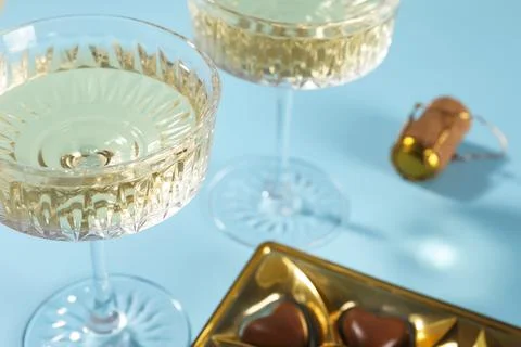 Glasses of expensive white wine and heart shaped chocolate candies on light b Stock Photos