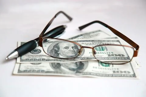 Glasses in a frame are on dollars with a black pen on a white table Stock Photos