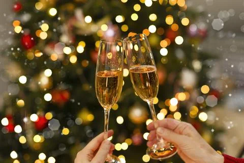 Glasses in hand close-up against the backdrop of Christmas lights and glare. Stock Photos