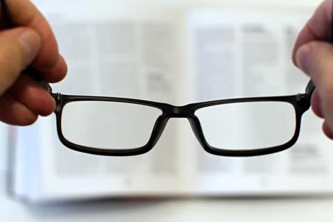 Glasses in hands on blurred background of open book Stock Photos