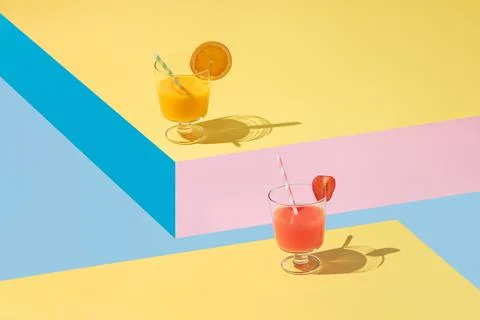 Glasses of orange and strawberry juice with pieces of fruit placed on geometric Stock Photos