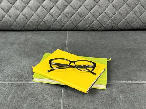 Glasses placed on notebook stack on sofa Stock Photos