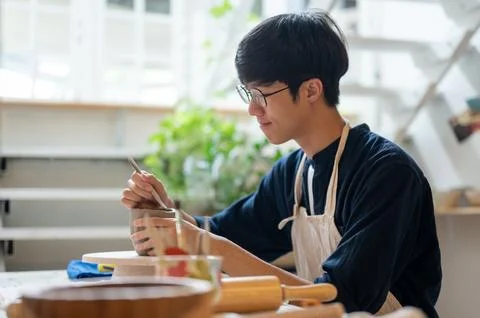 Glasses pottery artist using a throwing tool to make clay mug at working ta.. Stock Photos