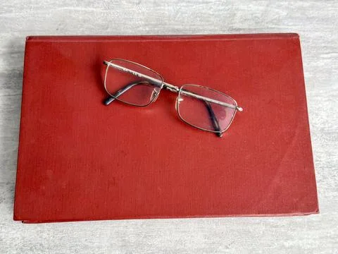 Glasses resting on a red book on a flat surface in a simple setup Stockfoto's