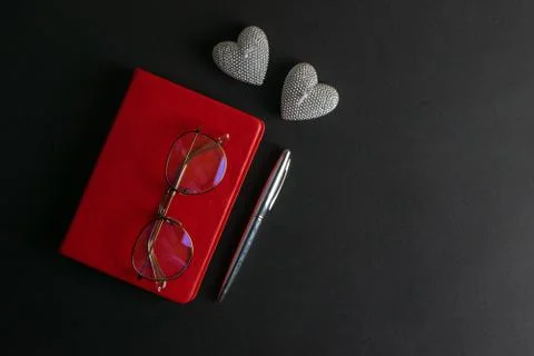 The glasses stand on a red notebook, there are two heart-shaped candles nearb Stock Photos