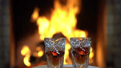 Glasses of whiskey slowly rotate in front of a burning cozy fireplace. Stock Footage 167525695