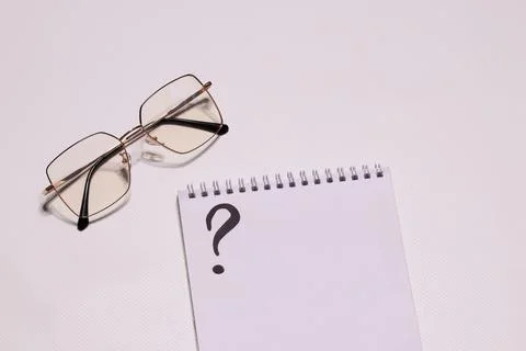 Glasses on a white background, next to a notebook with a question. Vision Stock Photos